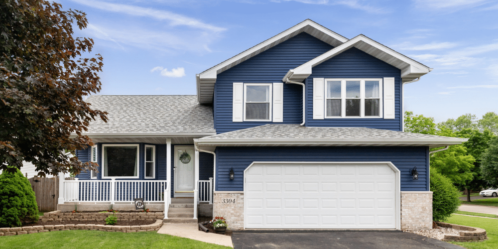 Two-story house with bright blue vinyl siding, white shutters, gray asphalt shingle roof, and a double-car garage in Central PA